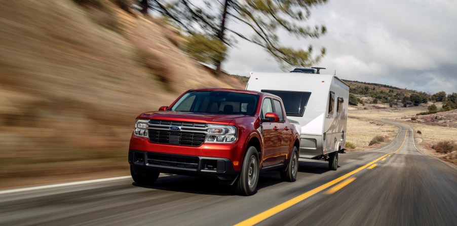 Promo shot of a red Ford Maverick towing a camper trailer up a hill.