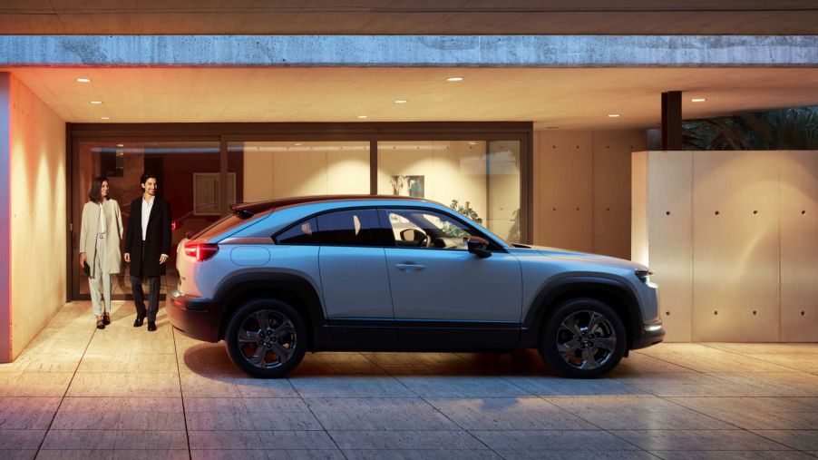 The 2022 Mazda MX-30 EV parked on a marble plaza right outside a building as a well-dressed couple approaches