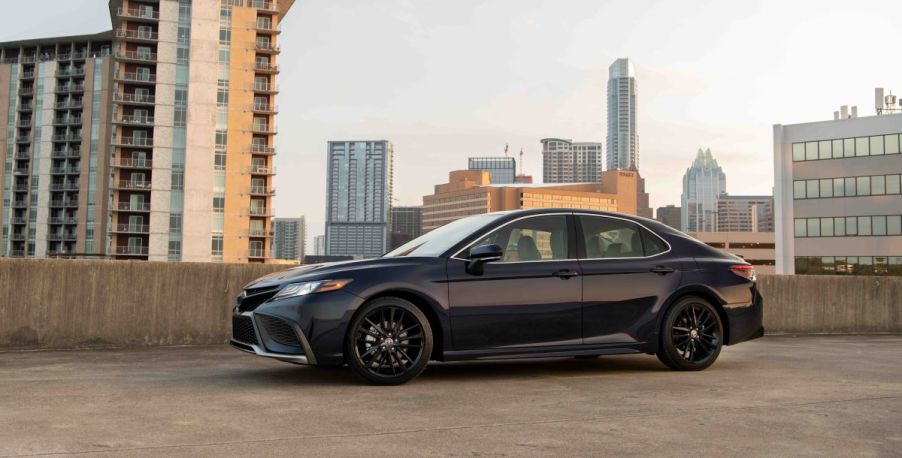 Eighth-gen Toyota Camry midsize sedan in black, parked on top of a concrete parking structure. Both the 2023 Camry and 2022 Camry have the same exterior styling.