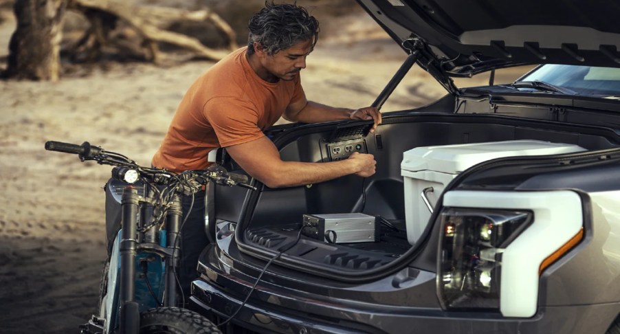 A person is inflating a tire using a gray 2022 Ford F-150 Lightning Mega Power Frunk.