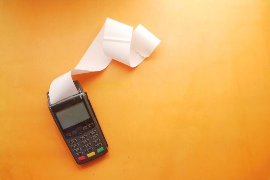 A black adding machine with a strip of black machine tape coming out, laying on an orange tape; calculating car financing rates is an important part of the buying process