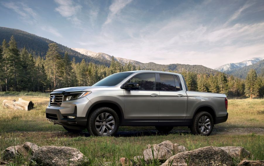 The 2022 Honda Ridgeline Sport pickup truck parked in a grassy field near hills of forest trees