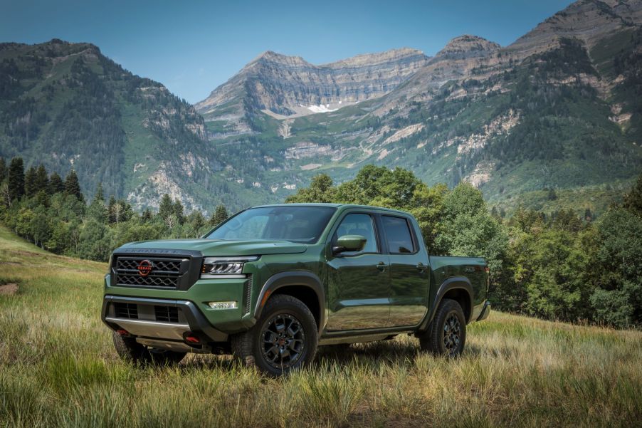 A green 2022 Nissan Frontier compact pickup truck with 9.4 inches of ground clearance parked near a mountain range forest