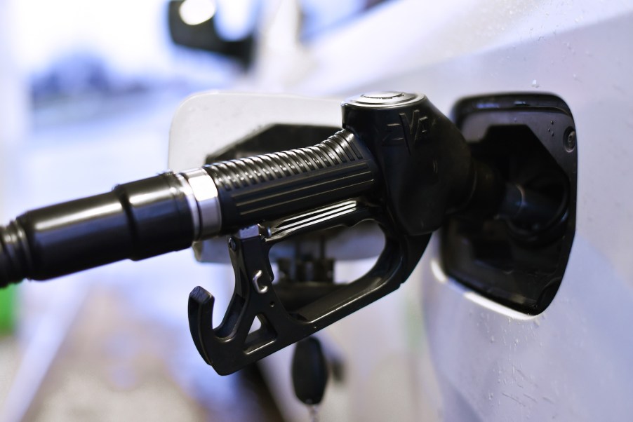 A white car being filled up by a black gas pump as gas prices continue going up.