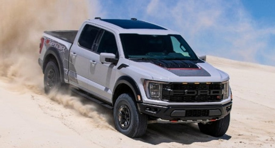 A white 2023 Ford F-150 Raptor R pickup truck is driving in the sand.