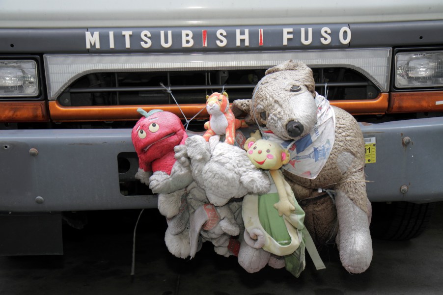 A stack of stuffed animals decorating the front bumper of a MIstubishi Fuso.