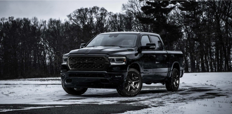 A black 2022 Ram 1500 full-size pickup truck parked on grass covered snow near barren trees