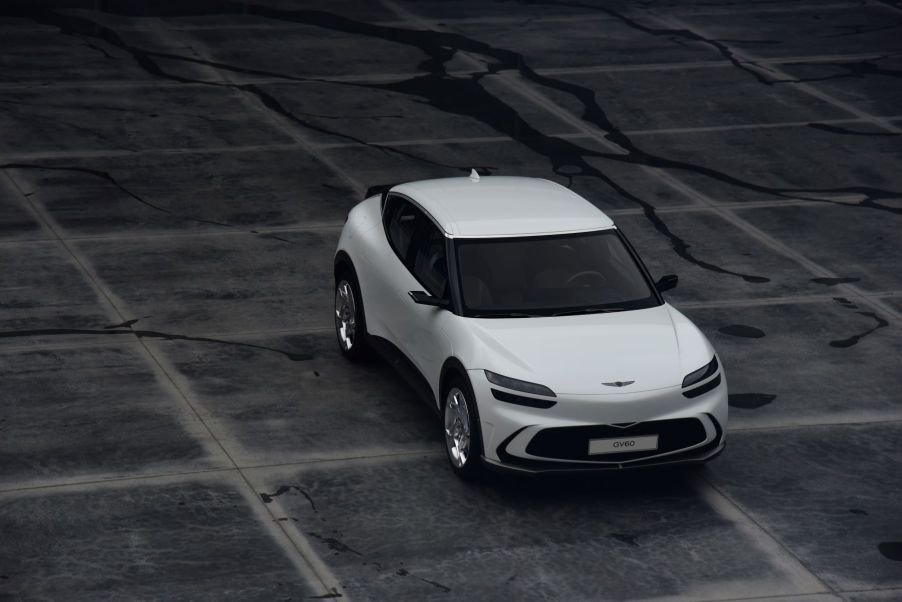 An overhead shot of a white 2023 Genesis GV60 electric SUV model parked on a cracked and stained ground of tiles