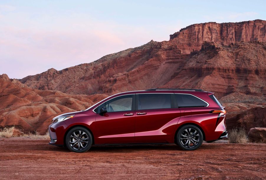 A 2022 Toyota Sienna minivan in Ruby Flare Pearl parked near orange mountains cliffs in the desert