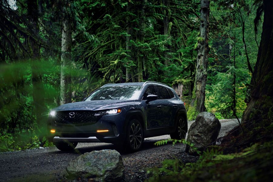 A 2023 Mazda CX-50 parked on a dirt trail within a deep green forest