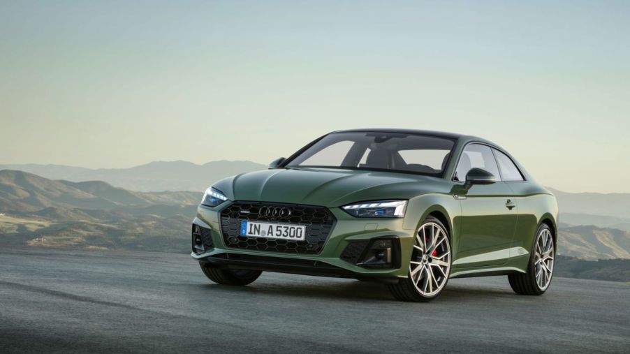 A green Audi A5 Coupe luxury car model parked on a asphalt in a terrain of hills covered in fog