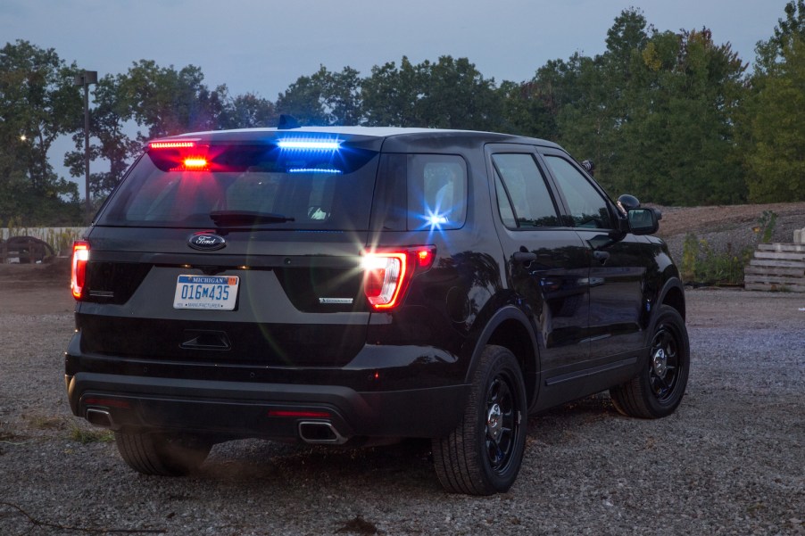 The rear of a black, unbadged Ford police SUV with a row of trees visible in the background.