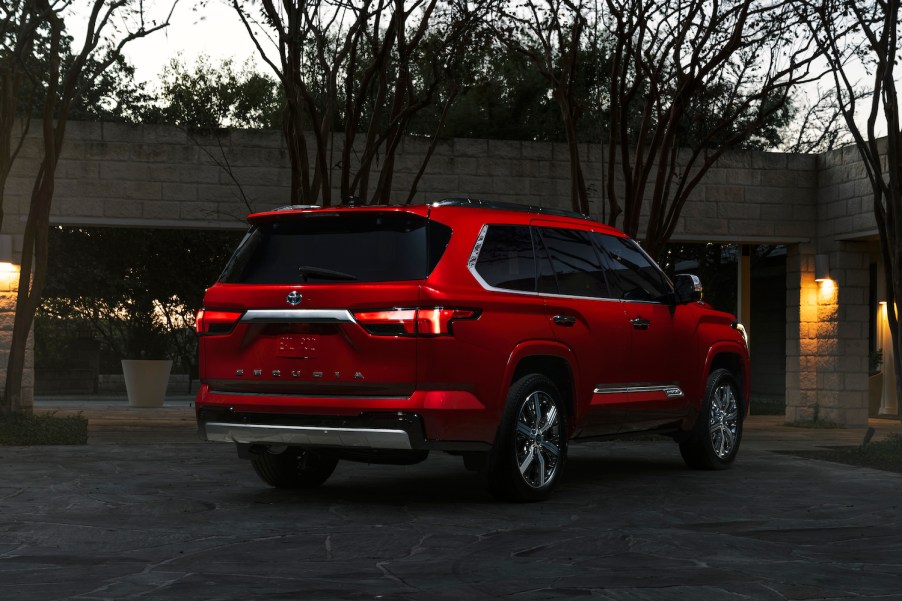 Red Toyota Sequoia full-size large hybrid SUV parked in a driveway at dusk.