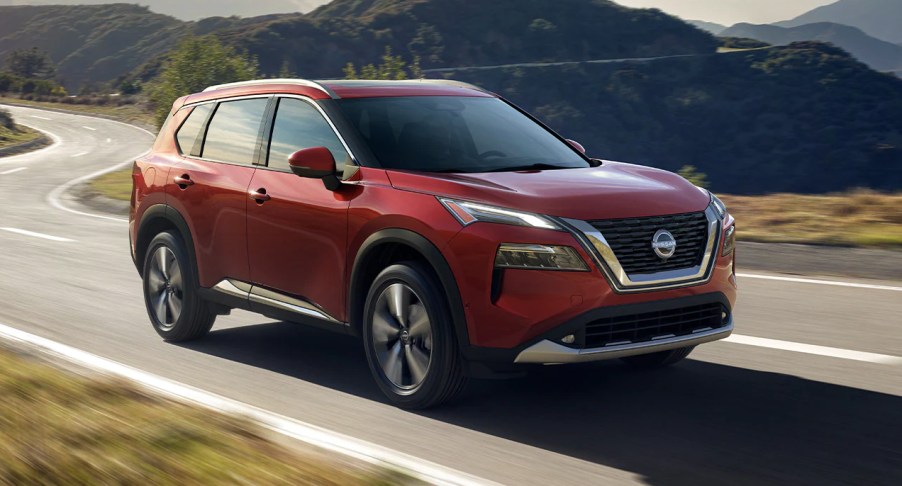 A red 2023 Nissan Rogue is driving on the road.