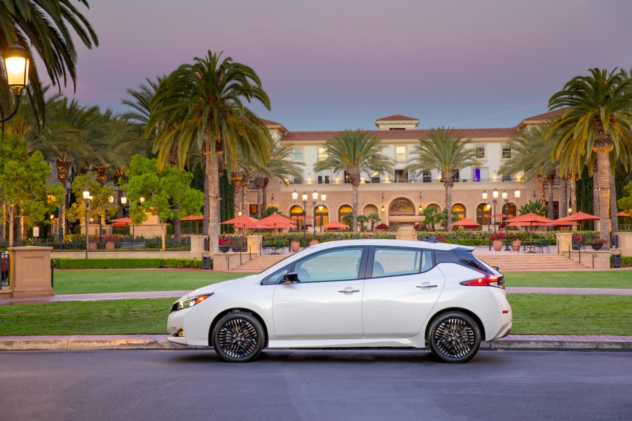 A white 2023 Nissan Leaf in front of a building in a tropical area.