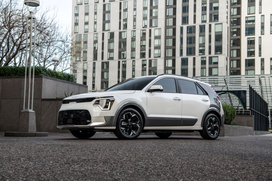 A white 2023 Kia Niro EV parked on a gravel/asphalt pavement near a lamppost