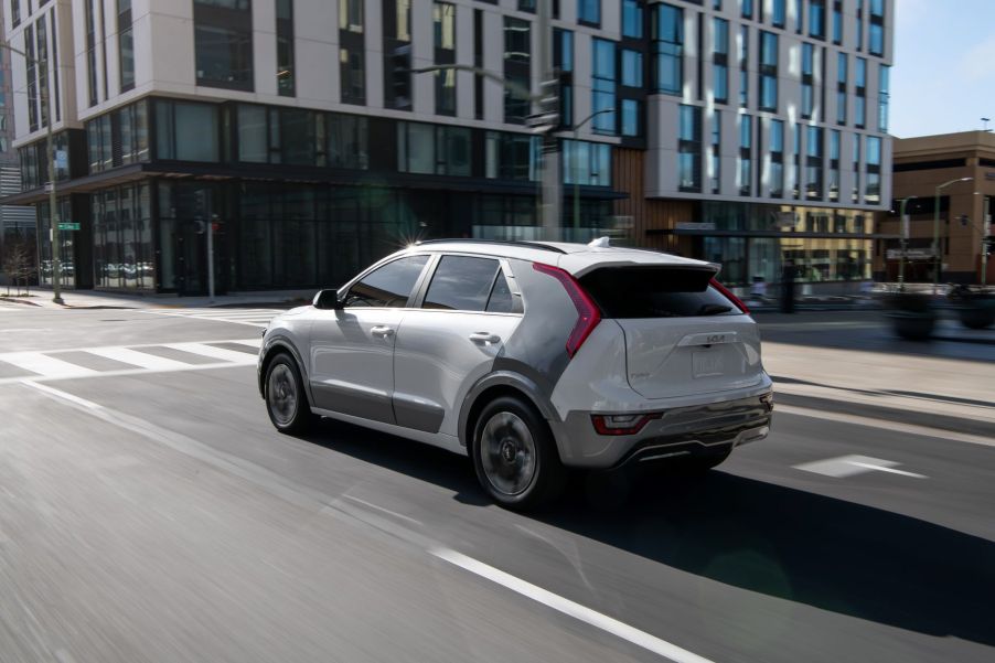 A white 2023 Kia Niro EV electric compact SUV model driving through an urban city near a set of streetlights