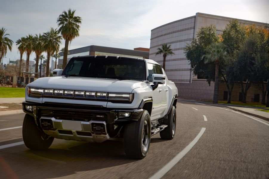 A white GMC Hummer EV electric pickup truck driving past palm trees