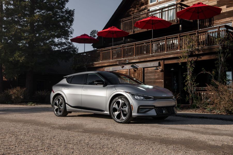 A silver-gray 2023 Kia EV6 compact electric SUV model parked on a gravel lot outside a wooden restaurant