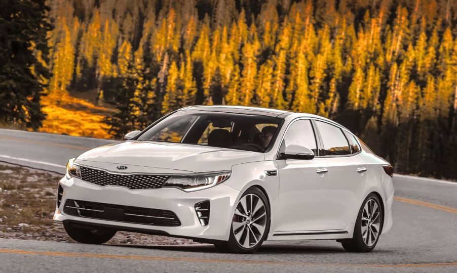 A white 2016 Kia Optima driving down an open road.