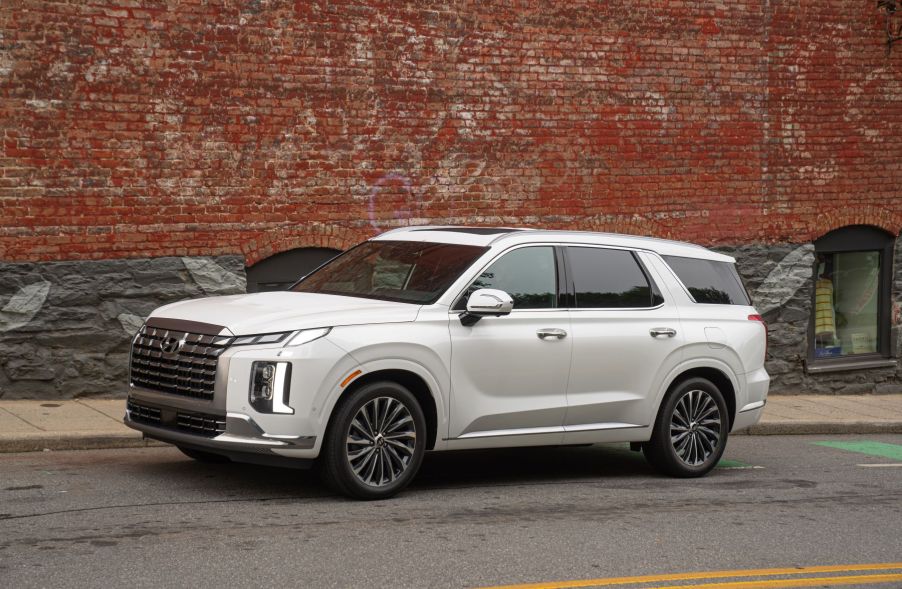 A white 2023 Hyundai Palisade midsize crossover SUV model parked on a street next to a red brick wall