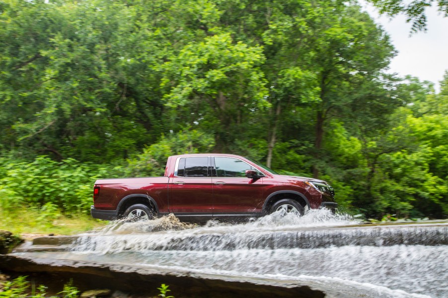 A Honda Ridgeline pickup truck fording a river, trees visible in the background.