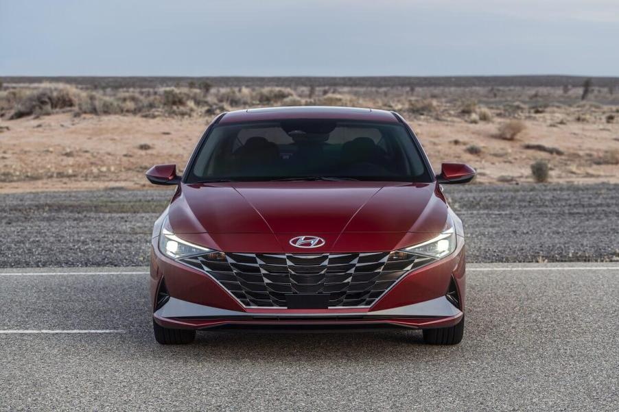 A new red 2023 Hyundai Elantra shows off its LED lights while it parks away from cars on a desert road.