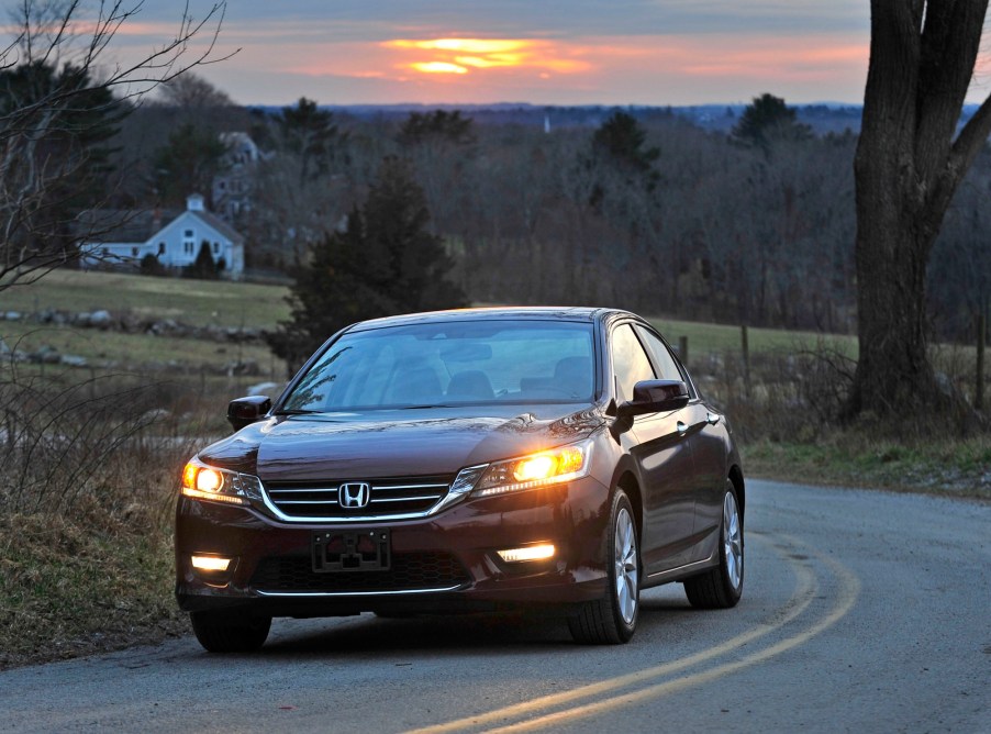 A used maroon Honda Accord car corners on a country road.