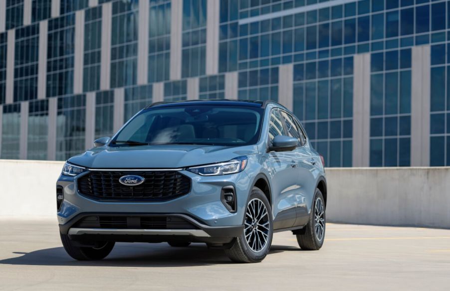 A light blue 2023 Ford Escape PHEV sits in front of a corporate building in bright daylight.