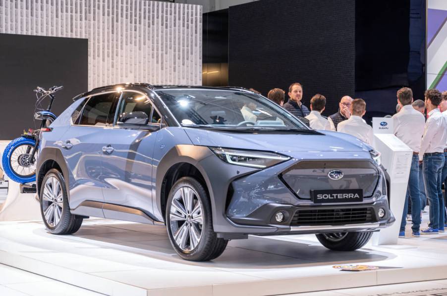 A blue 2023 Subaru Solterra EV SUV on display at an auto show with people around it.