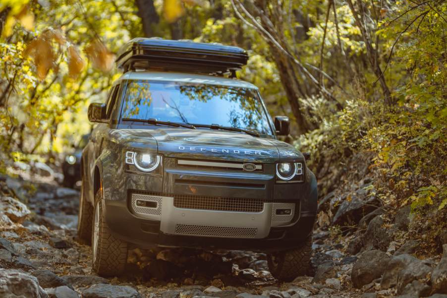 Head-on view of a Land Rover Defender traversing a rocky and heavily wooded trail.