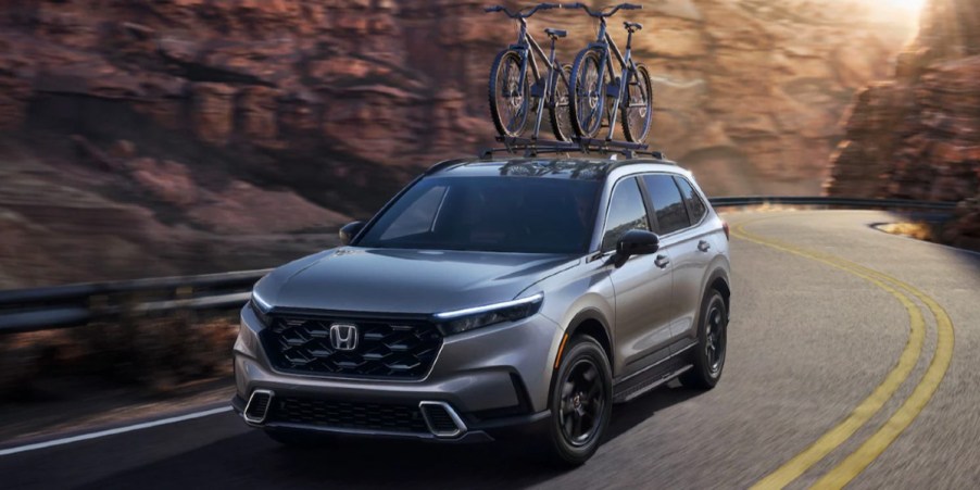 A gray 2023 Honda CR-V Hybrid small hybrid SUV is driving on the road.