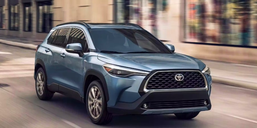 A blue 2023 Toyota Corolla Cross subcompact SUV is driving on the road.