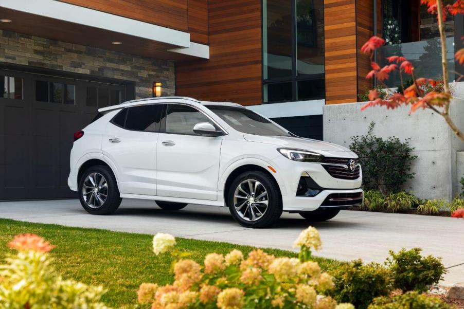 A white 2023 Buick Encore GX subcompact SUV model parked on a driveway of a luxury house near flowers