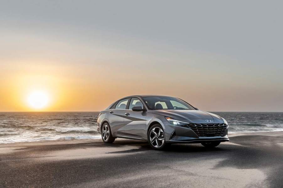 A grey 2023 Hyundai Elantra Hybrid parked in front of a sunset on a beach, one of the best small cars of 2023.