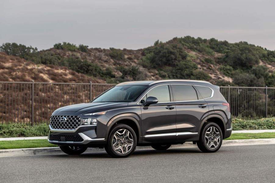 A dark grey 2023 Hyundai Santa Fe parked in front of a grassy hill on blacktop.