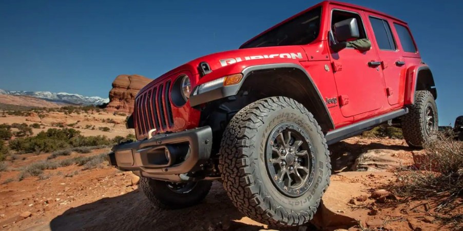 A red Jeep Wrangler small SUV is driving off-road.