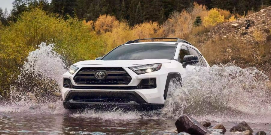 A white 2023 Toyota RAV4 small SUV is driving through water.