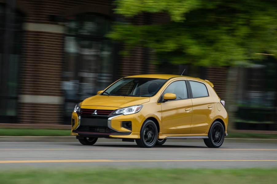 A yellow Mitsubishi mirage, one of the last cheap new cars on the market, drives down a street.