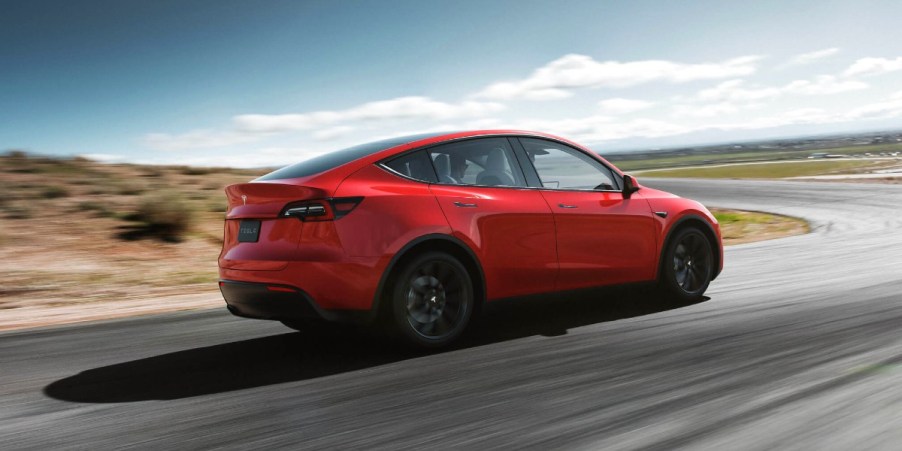 A red 2023 Tesla Model Y small electric SUV is driving on the road.