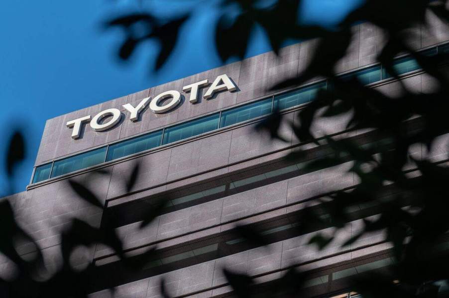 A Toyota logo seen through trees on a building in front of blue skies.