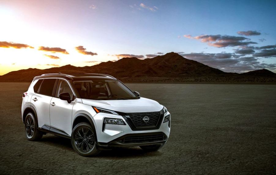 A white 2023 Nissan Rogue compact SUV model parked on dry and empty terrain in front of a sunset above a mountain