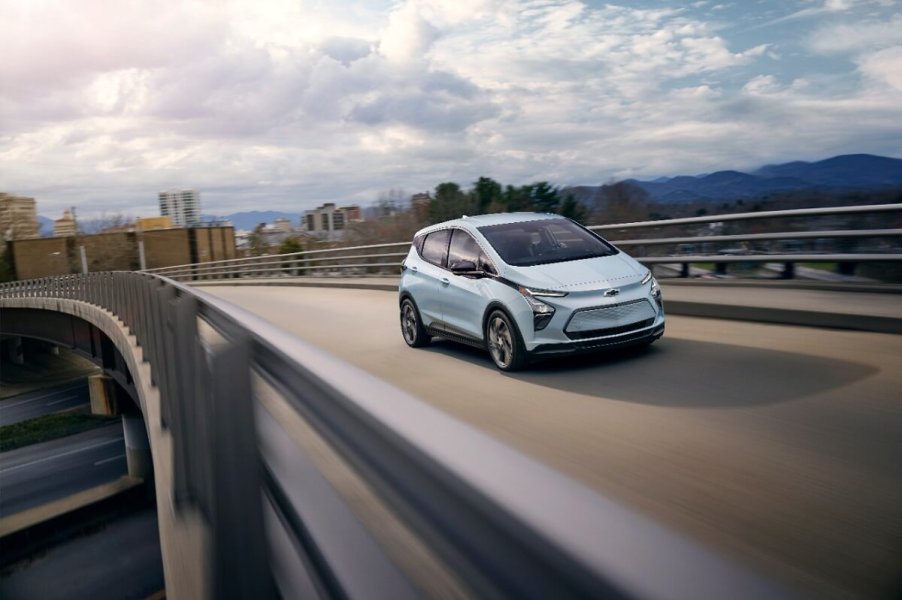 A light blue 2023 Chevy Bolt EV electric car cruises down a highway.