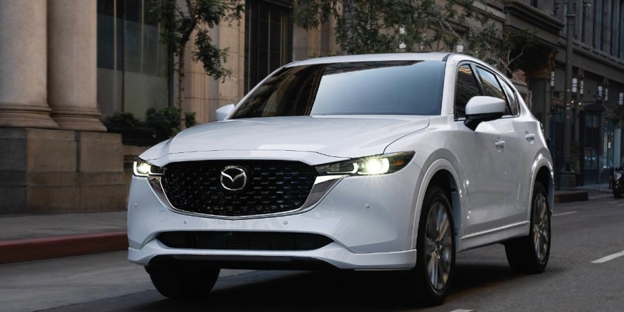 A white 2023 Mazda CX-5 small SUV is driving on the road.