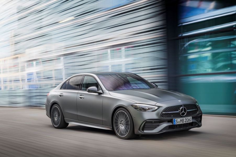 A gray 2023 Mercedes Benz C-Class driving next to a tall glass building