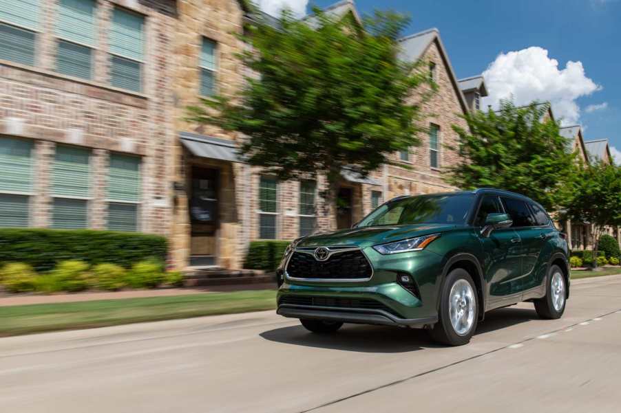 A green 2023 Toyota Highlander drives in front a limestone building.