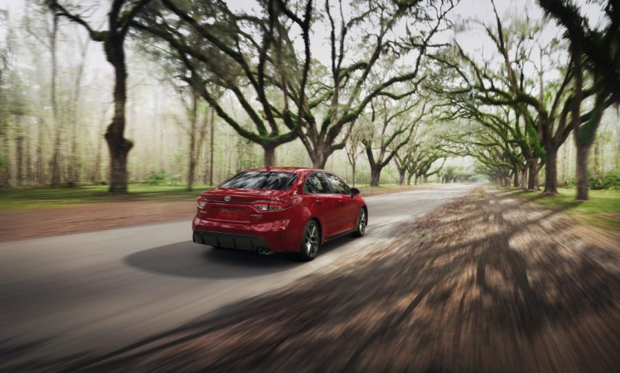 a red Toyota Corolla Hybrid driving through a tree-lined road