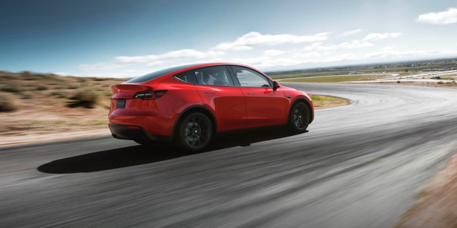 A red 2023 Tesla Model Y small electric SUV is driving on the road.