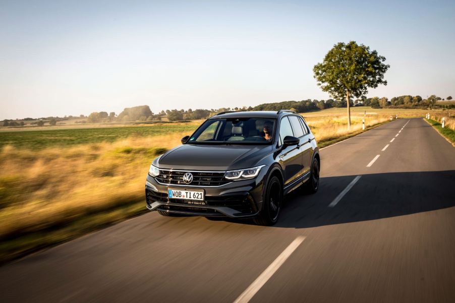 A gray 2023 Volkswagen Tiguan drives down a road with grass and a tree in the background. The Tiguan is the cheapest three-row SUV of 2023.