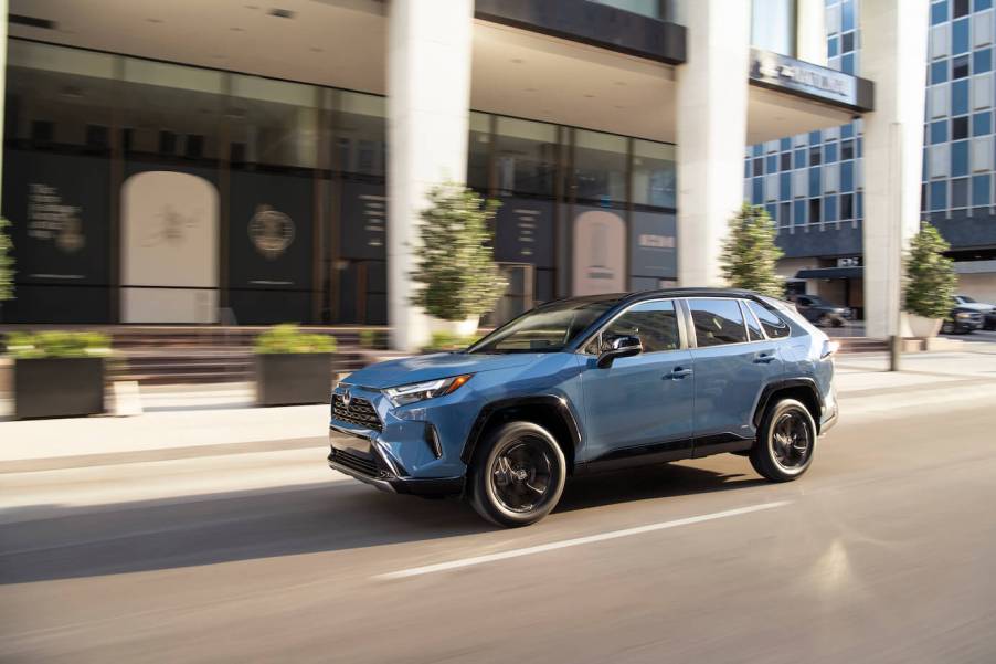 A blue Toyota RAV4 driving down a city block with business buildings in the background.